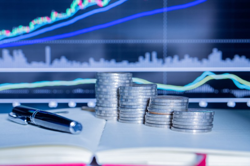 Stack of coins in front of a scrap metal prices trading graph